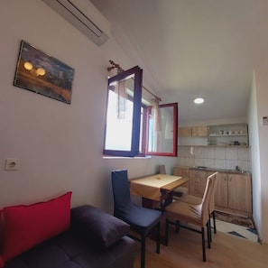 A compact living space with a dining area, kitchenette, and a sofa with a red cushion. - Apartments Tisno - one bedroom (right) (Tisno)