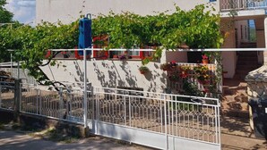 A two-story building with a flat roof, two windows with red shutters, and a balcony with a metal railing. - Apartments Tisno - one bedroom (left) (Tisno)