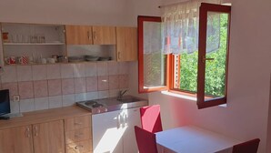A compact kitchen with a dining area, a window with lace curtains, and a tiled floor. - Apartments Tisno - one bedroom (left) (Tisno)