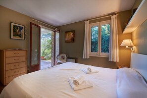 Ein Schlafzimmer mit einem Bett, einer Kommode, einem Stuhl, einem Fenster mit Vorhängen und einem Bild an der Wand.