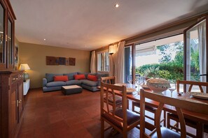Ein Wohnzimmer mit einer Couch, einem Esstisch, Stühlen und Blick auf Grünflächen.