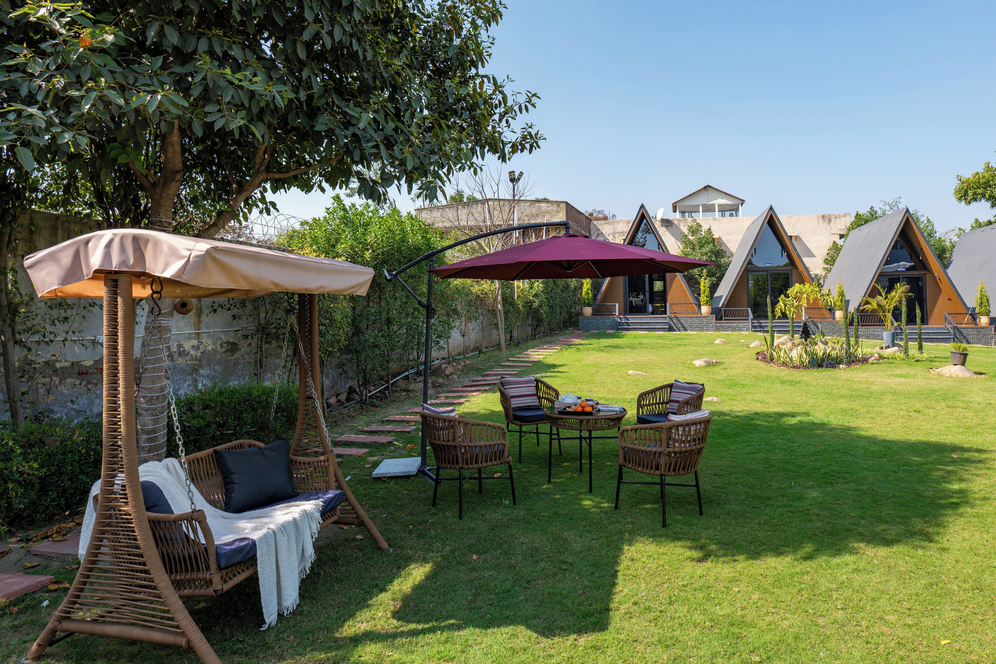 Un jardín con una silla mecedora, una mesa con sillas y un edificio con techo triangular.