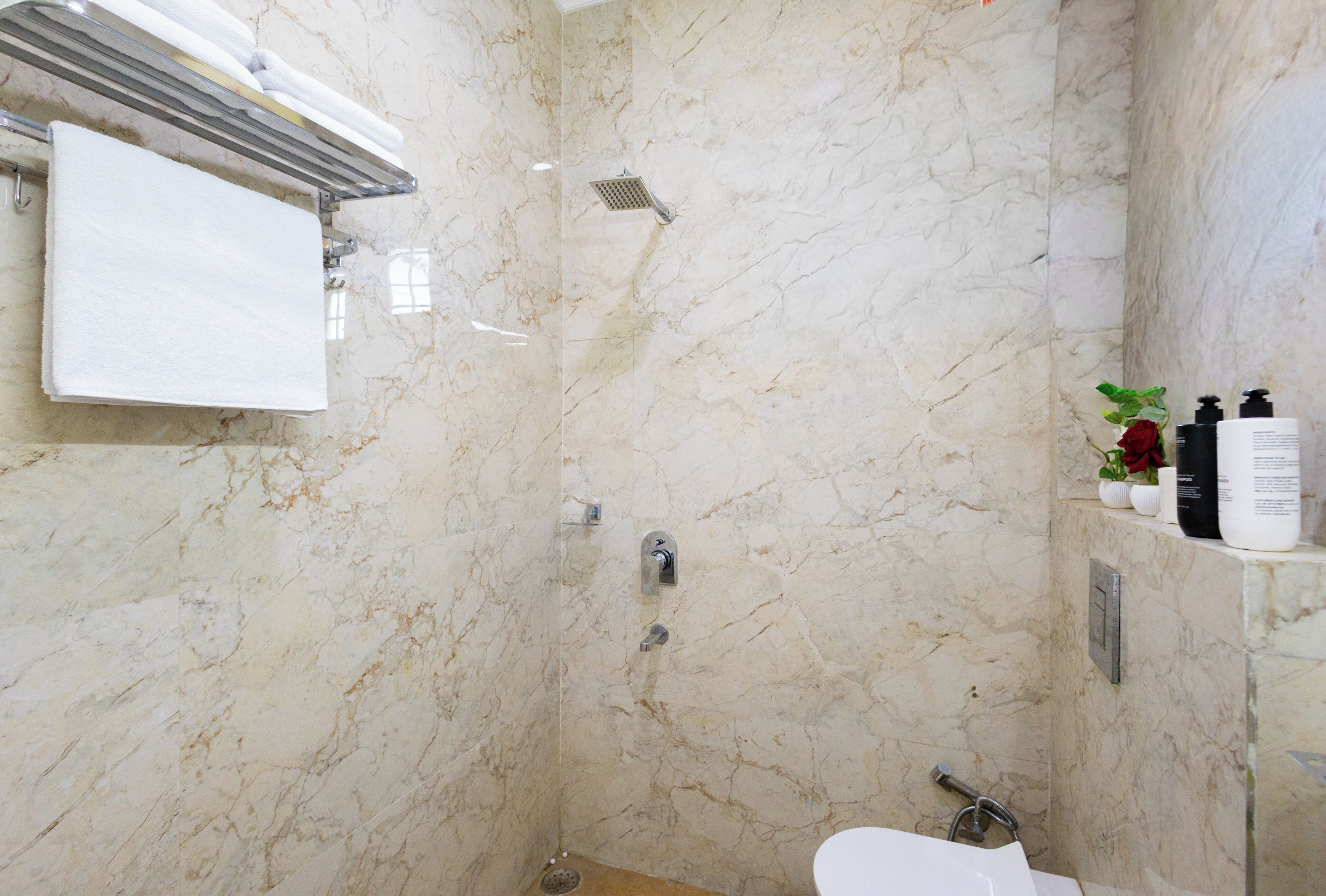 Een badkamer met een marmeren wand, een douche, een toilet en een handdoekhouder.