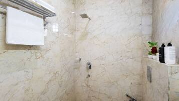 Een badkamer met een marmeren wand, een douche, een toilet en een handdoekhouder.