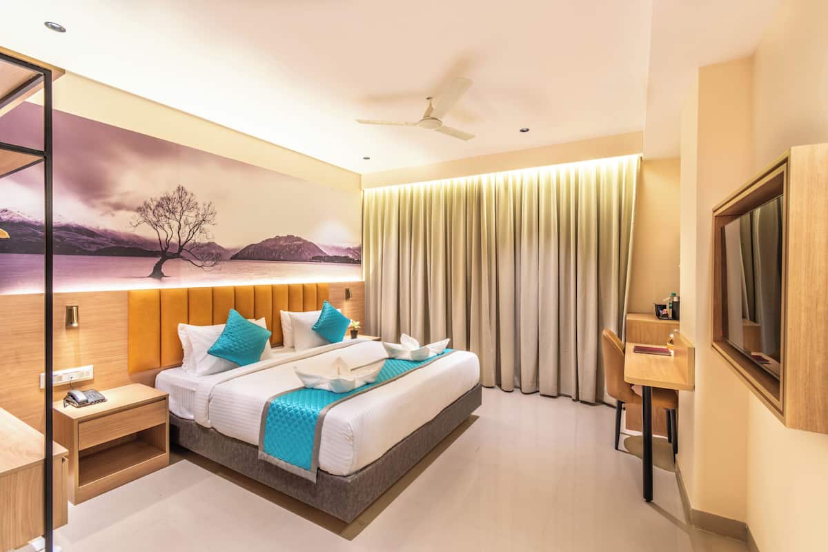 A modern hotel room with a large bed, a desk, a chair, a TV, and a painting on the wall.