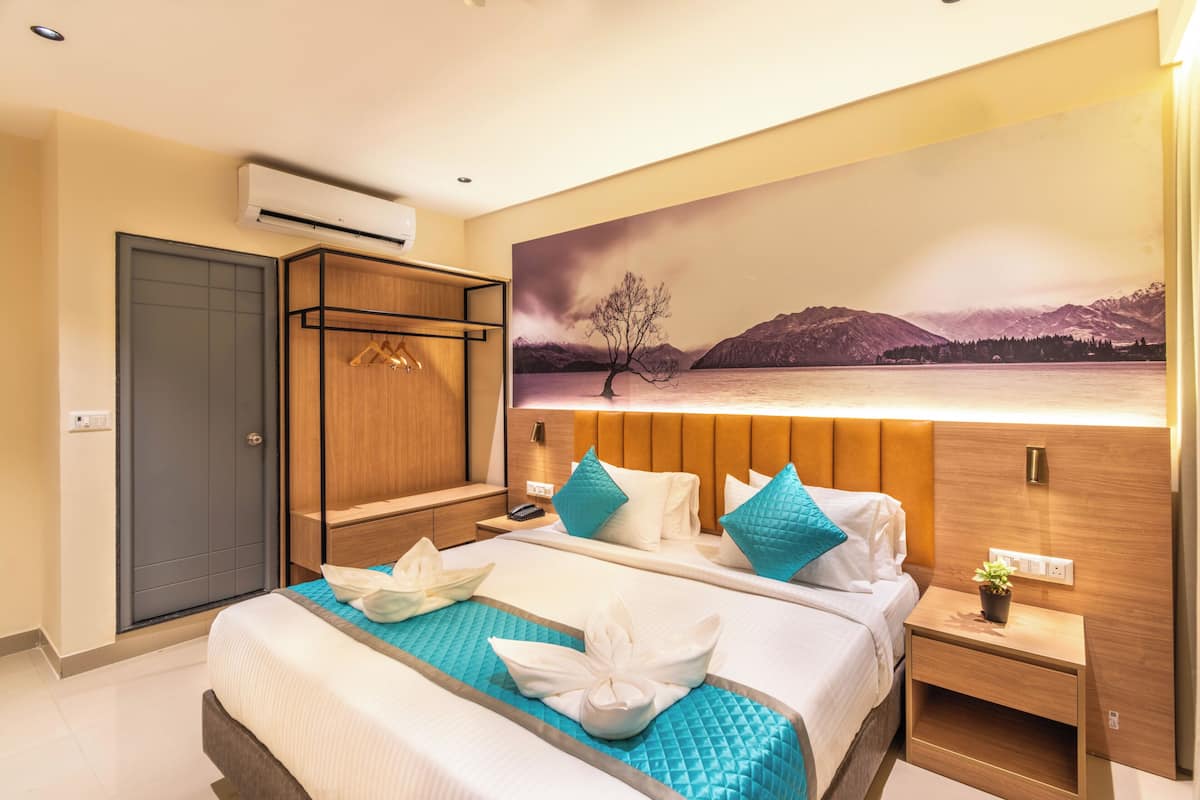 A hotel room with a bed, a wardrobe, a nightstand with a plant, and a painting of a landscape on the wall.