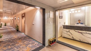 Et hotellets reception område med en marmor disk, en receptionist og en gang med døre samt potteplanter.