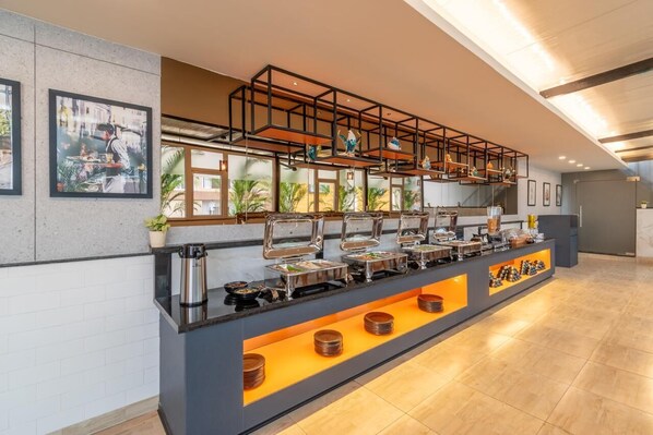 Montaje tipo bufé con varias estaciones de servicio, una máquina de café y un área de estar con vistas al exterior.