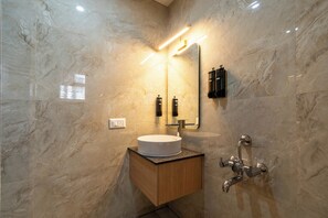 Un baño con pared de mármol, un lavamanos redondo, un espejo y una ducha.