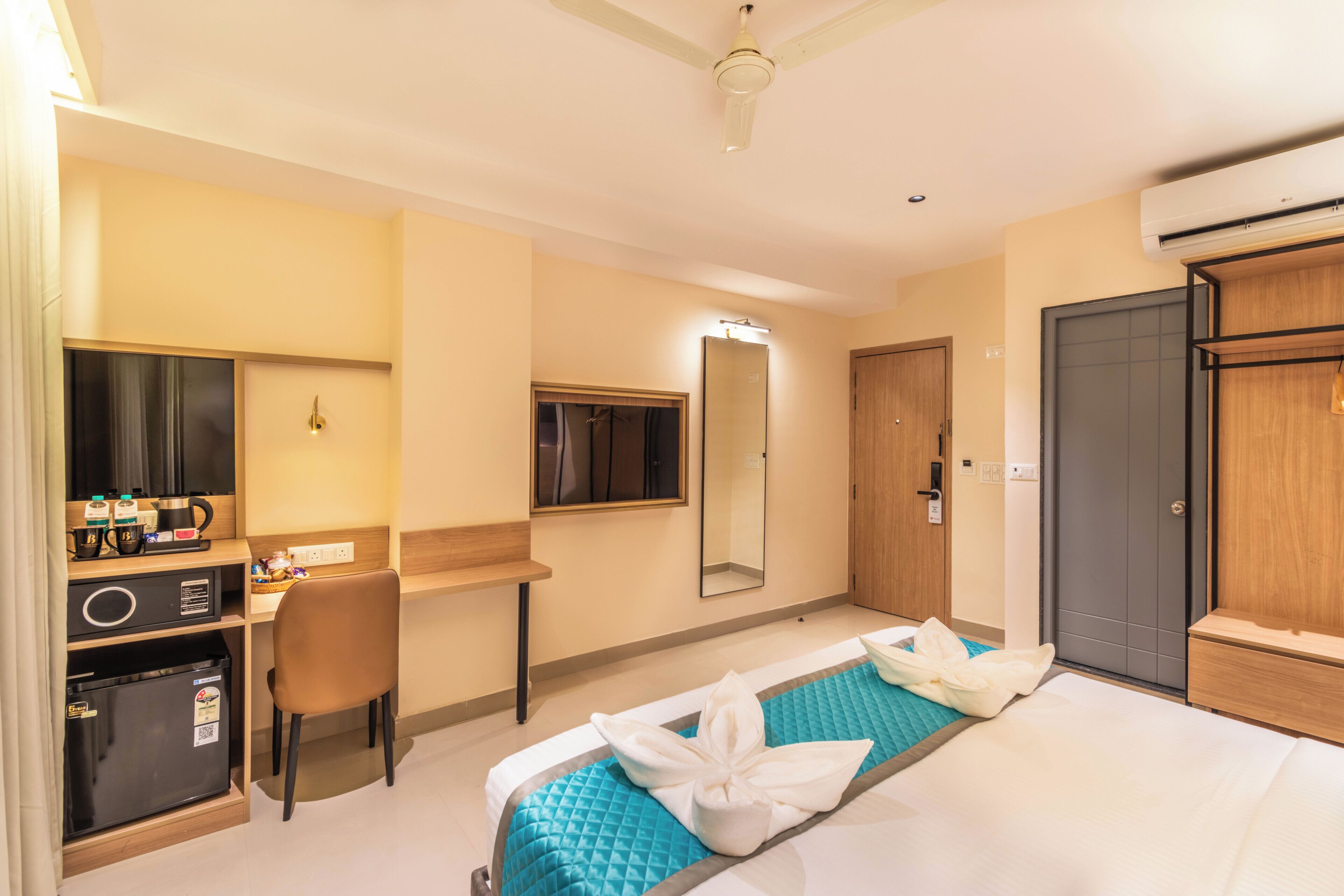 A hotel room with a bed, desk, chair, wardrobe, and a mirror.
