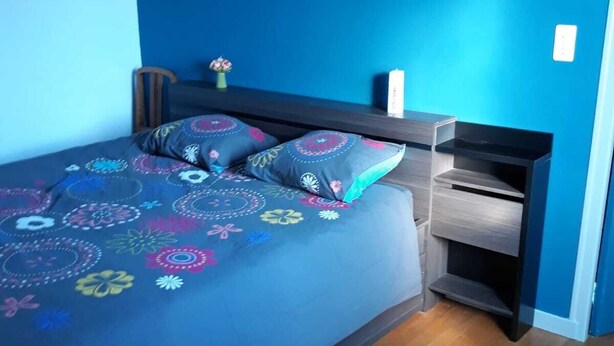 Un dormitorio con una cama, una mesita de noche, un estante en la pared y un cuadro enmarcado.