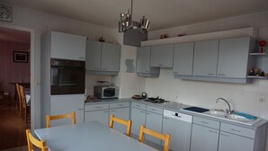 Una cocina moderna con armarios grises, horno integrado, microondas y lavavajillas. Hay una mesa de comedor con sillas y un reloj en la pared.