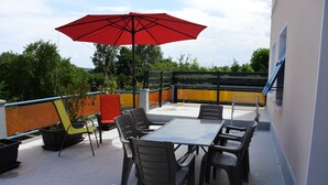 Terraza en la azotea con mesa y sillas, una sombrilla roja y plantas en macetas.