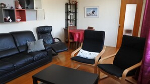 Una sala de estar con un sofá de cuero negro, un sillón negro, una mesa de centro de madera y una mesa de comedor con sillas.