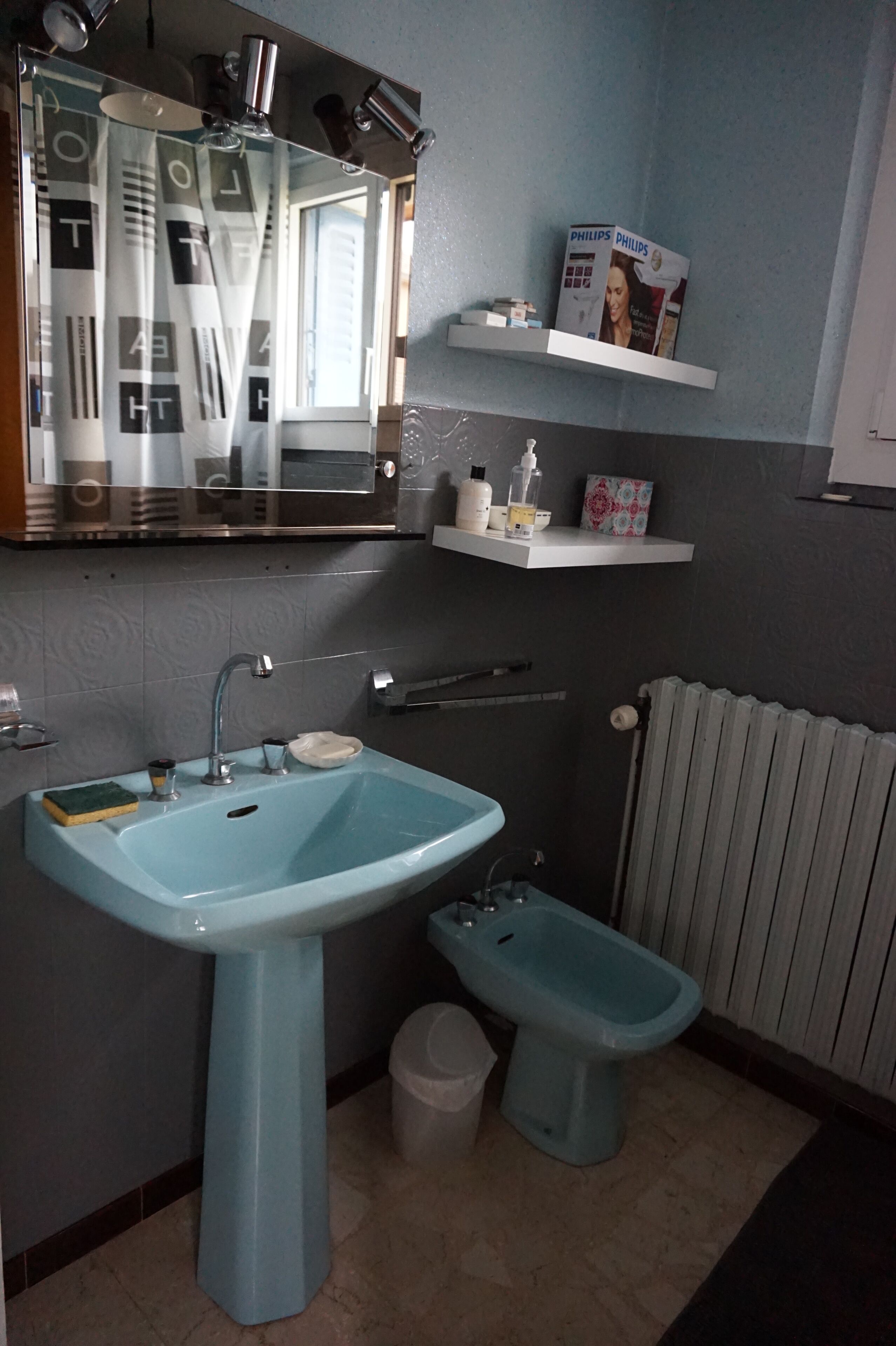 Ein Badezimmer mit blauem Waschbecken, einem Bidet, einem Spiegel und einem Ablagefach mit Pflegeprodukten.