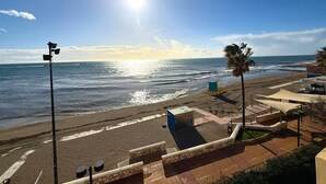 Blick auf einen Strand mit blauem Himmel, der Sonne, die sich im Wasser spiegelt, und einem Rettungsturm.
