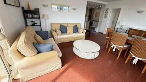 Ein Wohnzimmer mit einer Couch, einem runden Couchtisch und einem Essbereich mit Korbstühlen und einem Tisch.