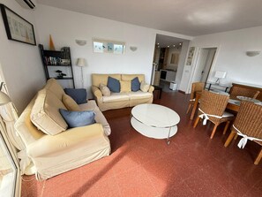 Ein Wohnzimmer mit einer Couch, einem runden Couchtisch und einem Essbereich mit Korbstühlen und einem Tisch.