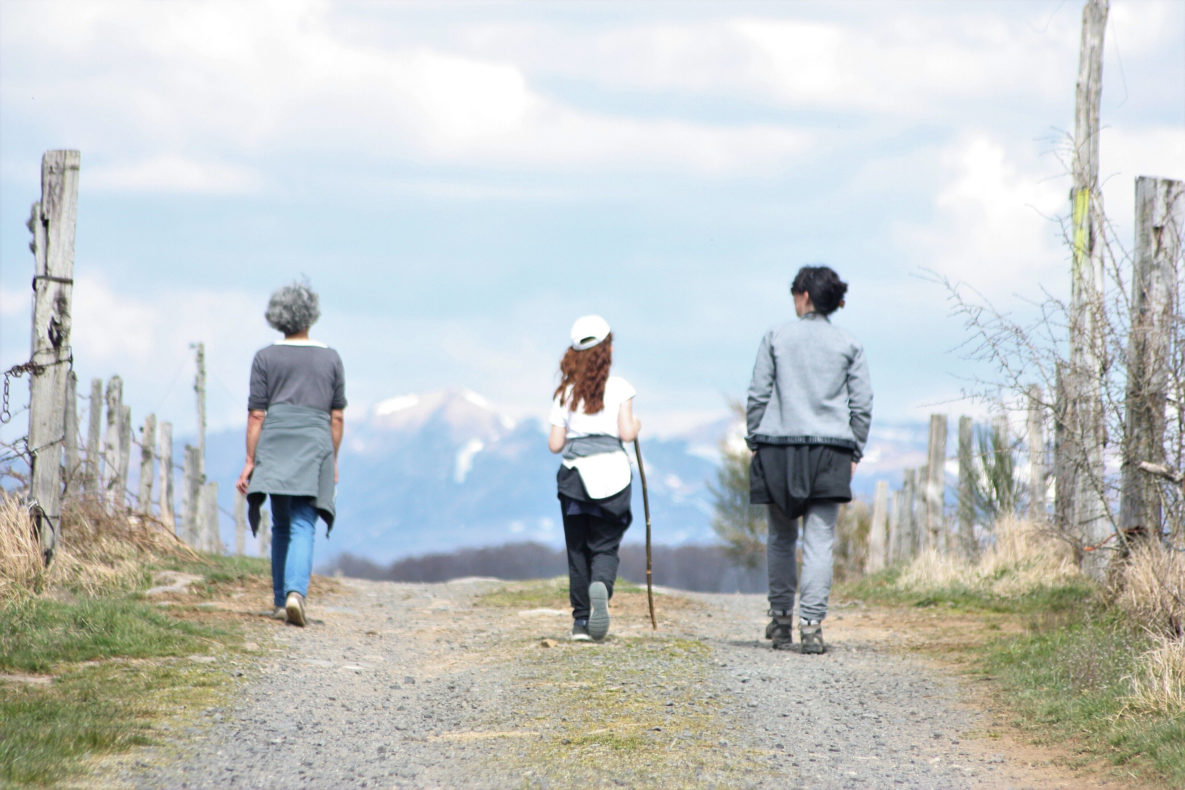 Three people walking on a gravel path with a wooden fence on one side and a mountain in the background.