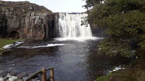 Une cascade se jetant dans une rivière, le tout entouré de falaises rocheuses et d’une végétation clairsemée.
