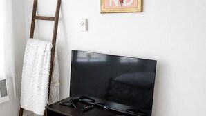 A room with a flat-screen TV on a dark wooden stand, a white towel hanging on a wooden ladder, a wicker basket, and a framed artwork on the wall. - Downtown Detroit Swanky Suite (Detroit)