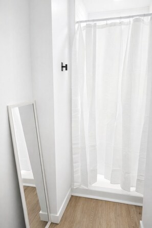 Un baño con cortina de ducha blanca, un espejo y suelo de madera.