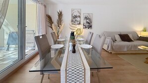 A dining area with a glass table, chairs, and a sofa. - L'Oasis Florentine - T2 - AC - Garden - WIFI (Fréjus)