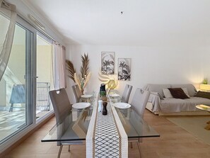 A dining area with a glass table, chairs, and a sofa. - L'Oasis Florentine - T2 - AC - Garden - WIFI (Fréjus)