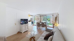 A living room with a sofa, a glass coffee table, a TV, and a dining area with chairs and a table. - L'Oasis Florentine - T2 - AC - Garden - WIFI (Fréjus)