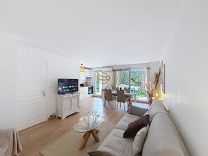 A living room with a sofa, a glass coffee table, a TV, and a dining area with chairs and a table. - L'Oasis Florentine - T2 - AC - Garden - WIFI (Fréjus)