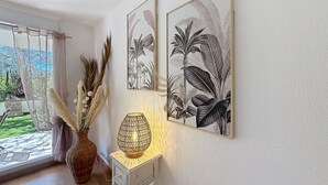 A room with a window, a vase with pampas grass, a table lamp, and two framed botanical prints on the wall. - L'Oasis Florentine - T2 - AC - Garden - WIFI (Fréjus)