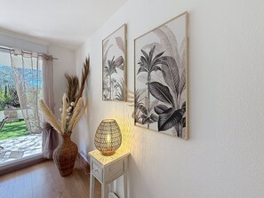 A room with a window, a vase with pampas grass, a table lamp, and two framed botanical prints on the wall. - L'Oasis Florentine - T2 - AC - Garden - WIFI (Fréjus)