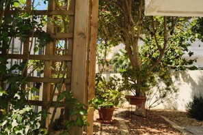 Una estructura de celosía de madera, plantas en macetas y un árbol en un jardín.