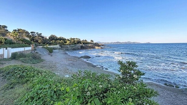 Un paisaje costero con playa rocosa, vegetación y cielo despejado.