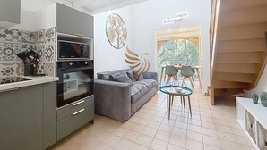 Un espacio habitable pequeño con kitchenette, un sofá gris, una mesa de comedor y una escalera.