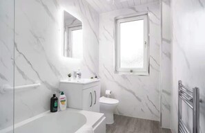 Un baño con pared de mármol, inodoro, lavabo, bañera y ventana.