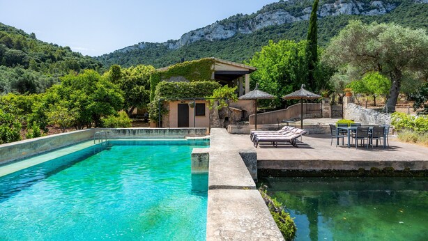 A swimming pool with lounge chairs and a table, surrounded by greenery and a mountain backdrop. - Authentic Mallorcan House with Pool and Sea Views (Son Ferrandell)
