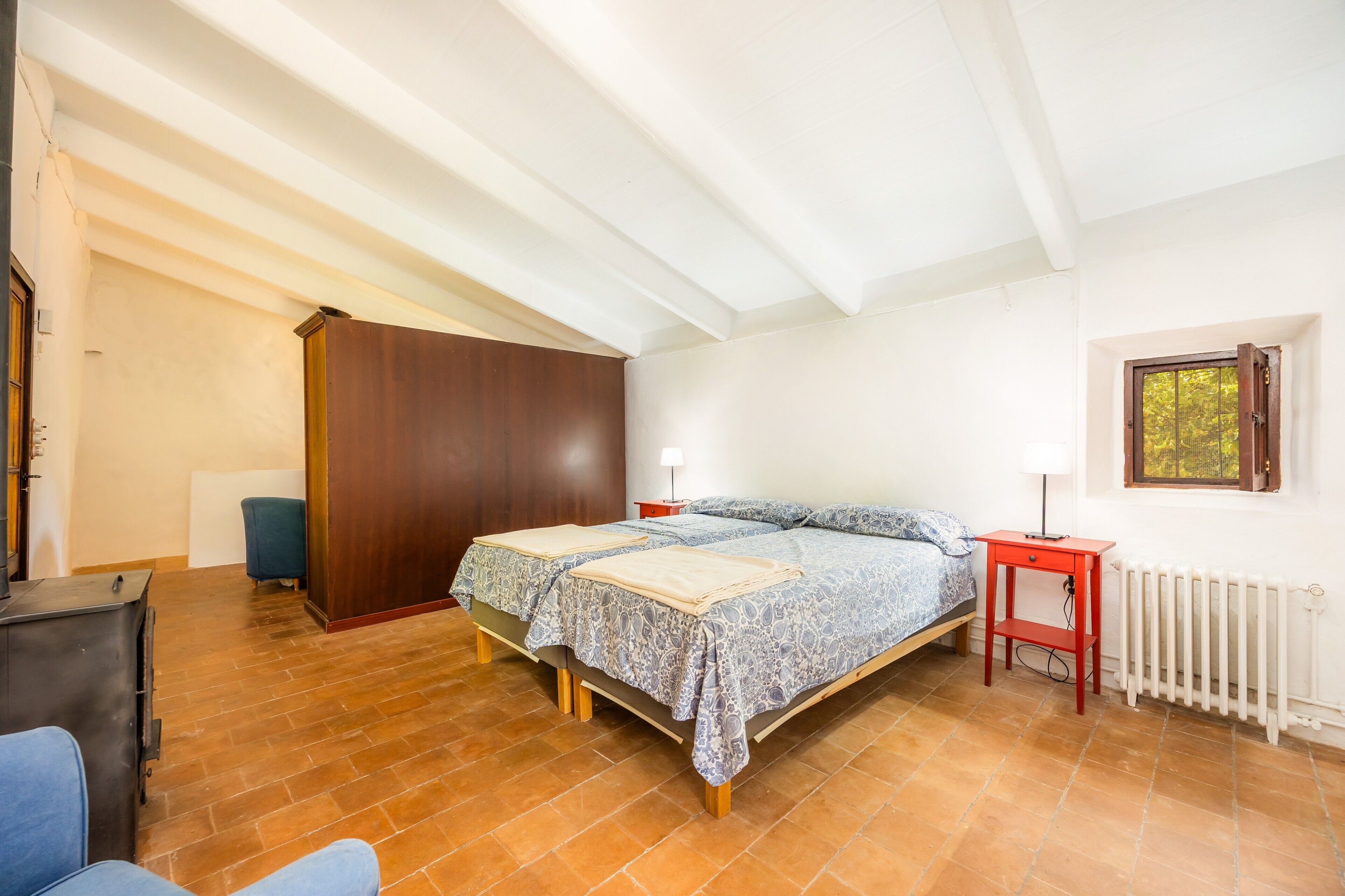 Een slaapkamer met een bed, een rode nachtkastje, een radiator en een raam.