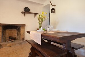 A dining area with a wooden table set for two, a fireplace, a clock, and a lantern on the wall.