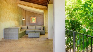 A covered patio area with wicker furniture, a lamp, and a view of greenery. - Authentic Mallorcan House with Pool and Sea Views (Son Ferrandell)