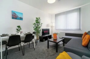 Ein modernes Wohnzimmer mit einer Couch, einem Fernseher, einem Esstisch mit Stühlen und einer Topfpflanze.