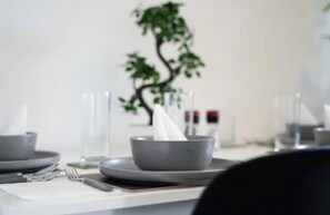 Una mesa de comedor dispuesta con platos, tazones y cubiertos, con una planta al fondo.