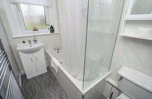 Un baño con ducha de vidrio, lavamanos blanco y retrete.