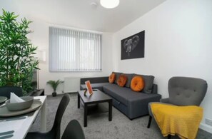 Una sala de estar moderna con un sofá gris, una mesita, un sillón gris y un ventanal con persianas.