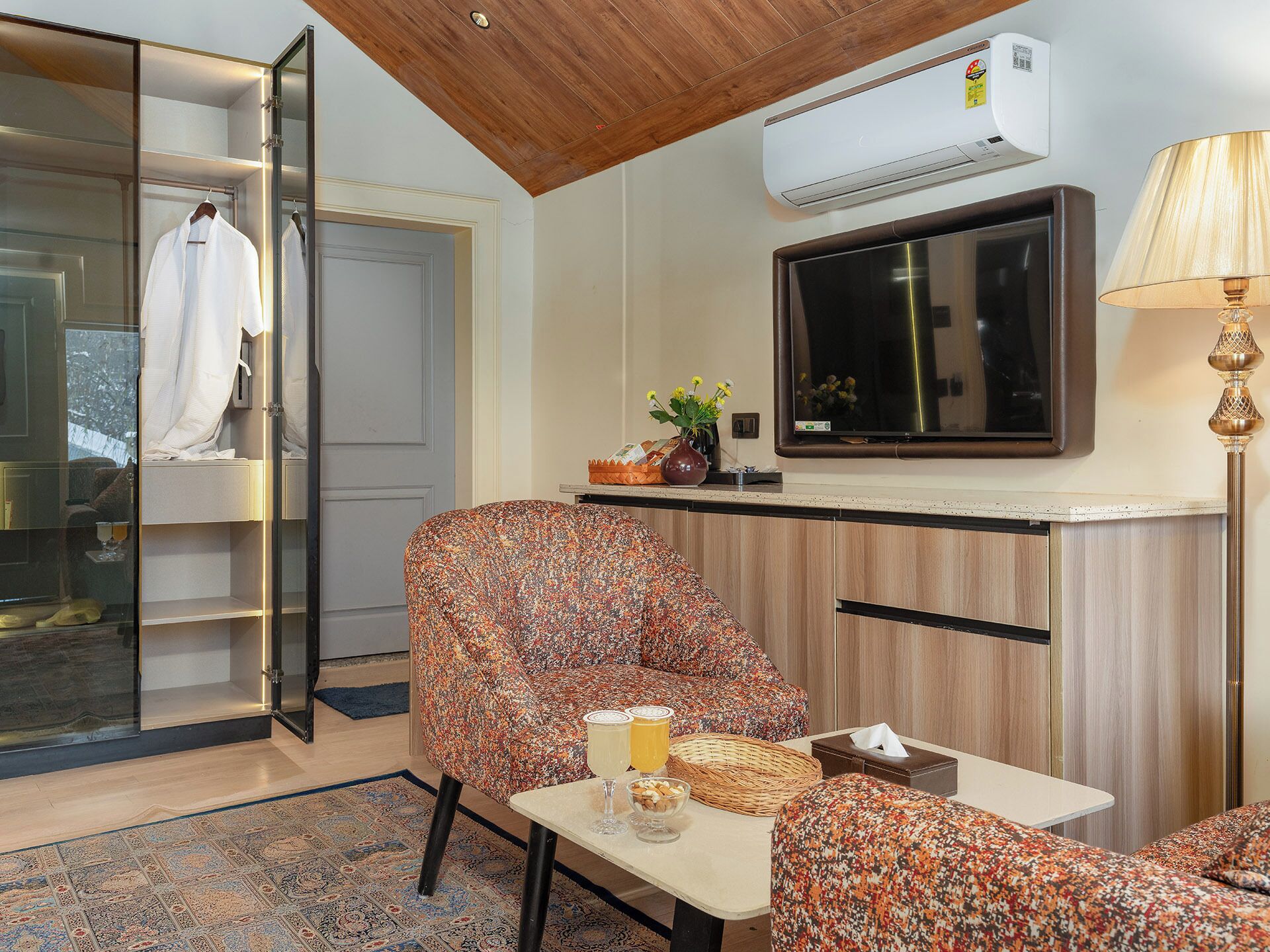 A room with a TV, a table with a glass of drink, a chair, a sofa, and a wardrobe.