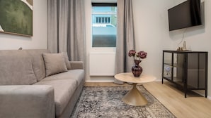 A modern living room with a sofa, a round coffee table, a vase with flowers, a TV on the wall, and a window with curtains. - Týsgata Apartments by Heimaleiga (Reykjavík)