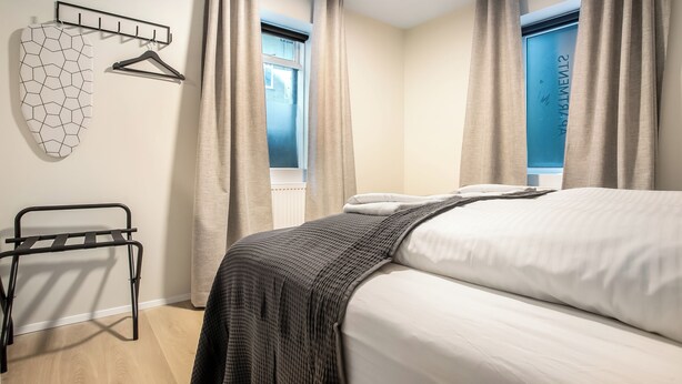 A bedroom with a bed, a hanging rack, a radiator, and a window with curtains. - Týsgata Apartments by Heimaleiga (Reykjavík)