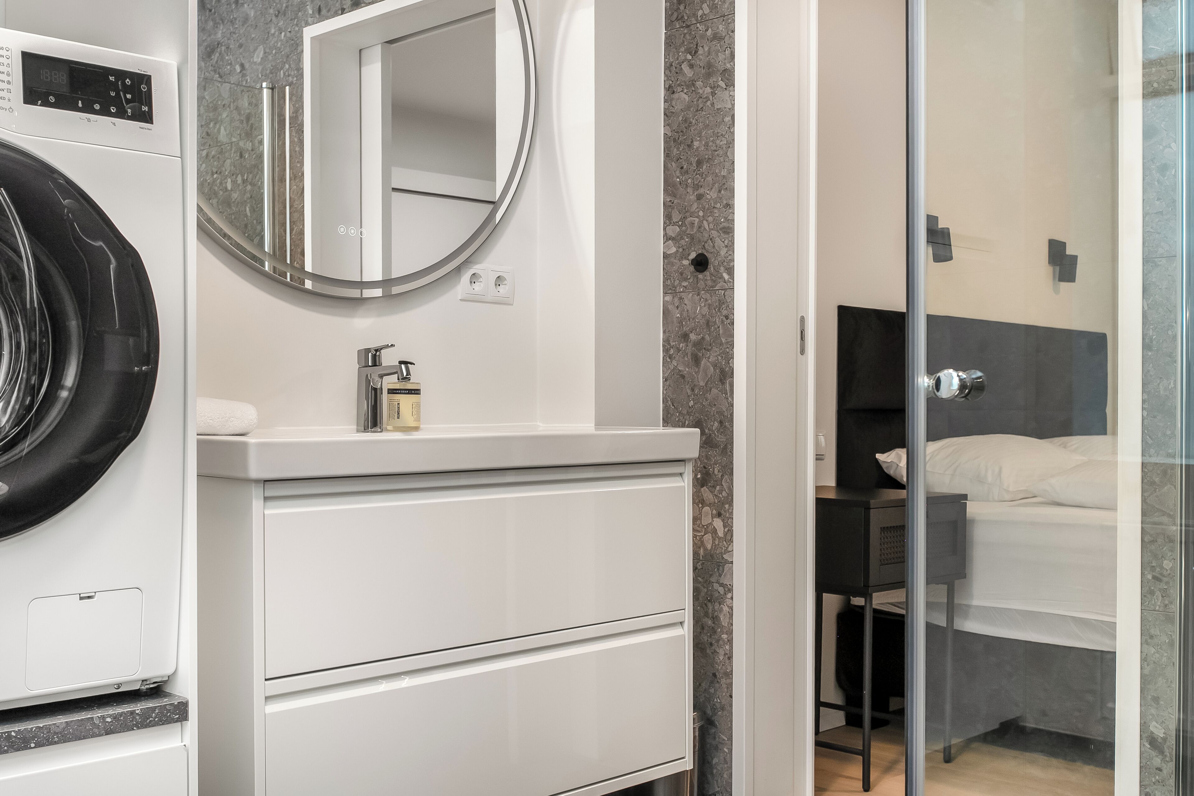 A modern bathroom with a washing machine, a mirror, a sink, and a shower area.