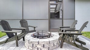 Un foyer est entouré de fauteuils Adirondack, et l’ensemble est installé sur une terrasse avec un bâtiment en arrière-plan.