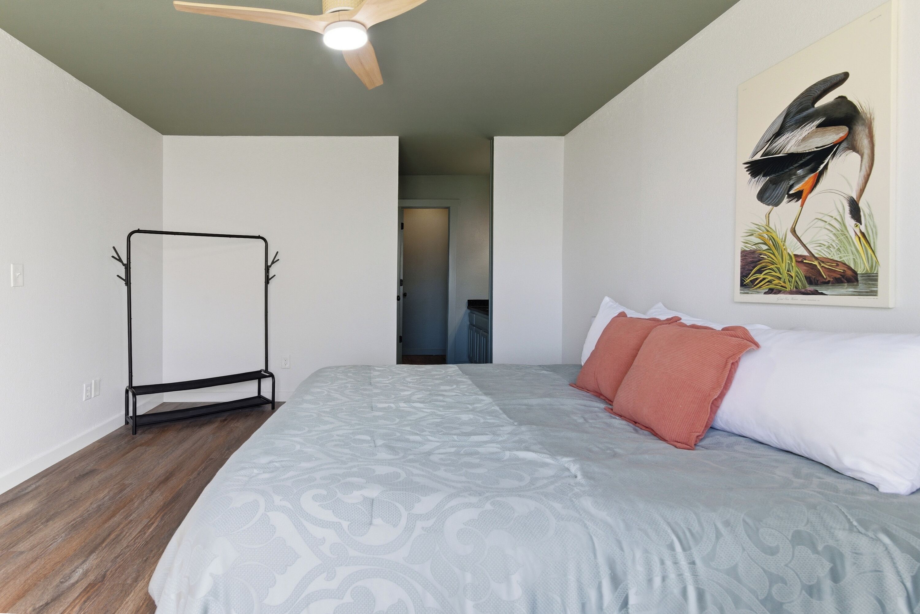A bedroom with a bed, a ceiling fan, a door, and a painting on the wall.